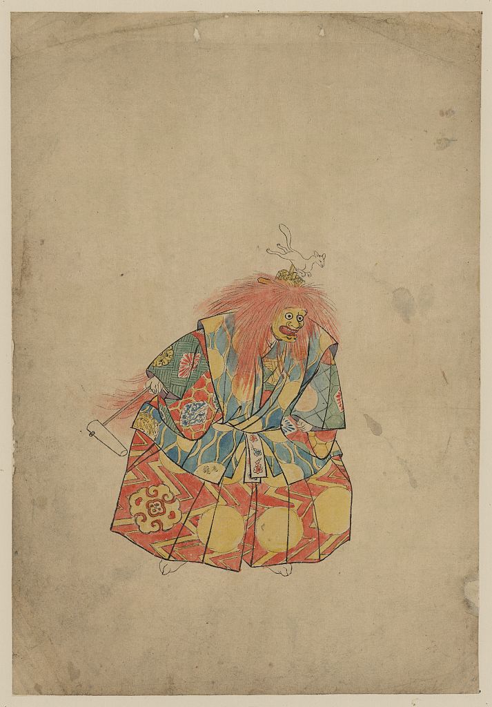 A picture of A clown wearing colorful costume and mask, with wild hair and hat with animal on top, and holding a rattle