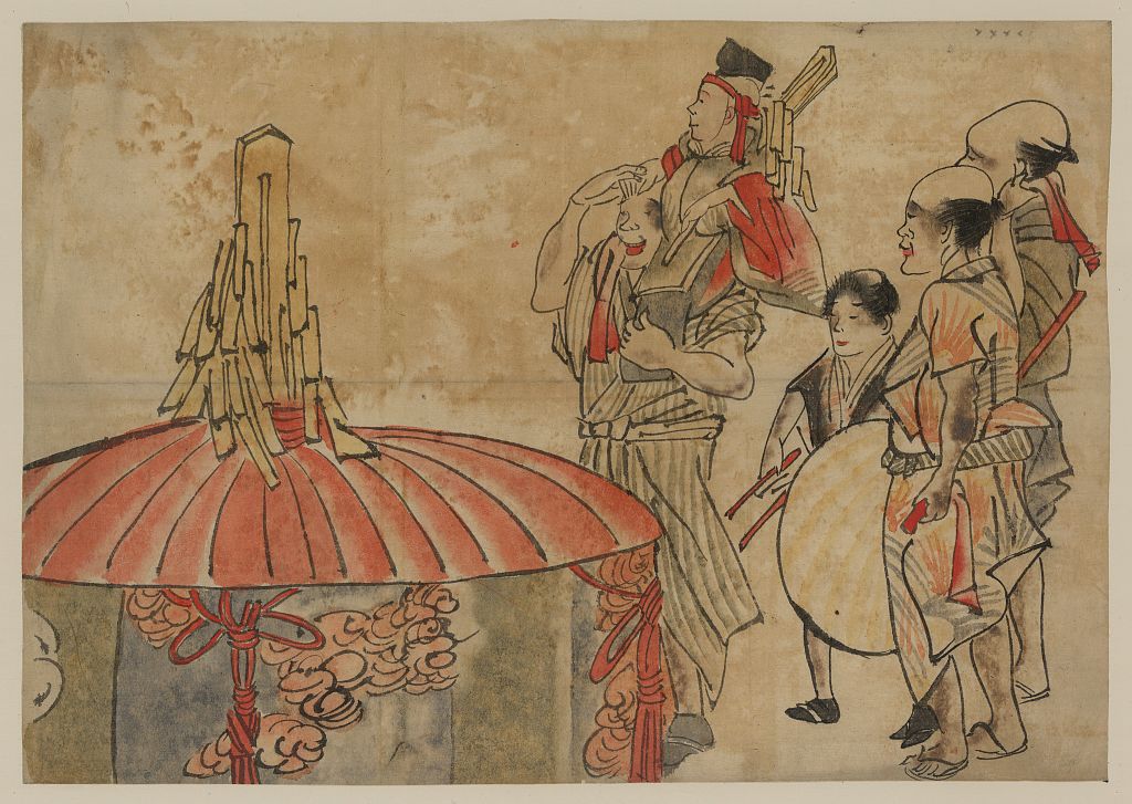A picture of Actors or musicians standing next to a large, decorated cylindar with cover; one man is carrying another on his shoulders